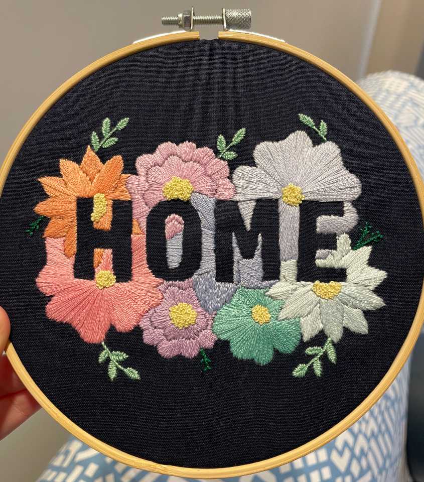 "Home" embroidery hoop utilising a negative space design. Pastel flowers on a dark blue background.