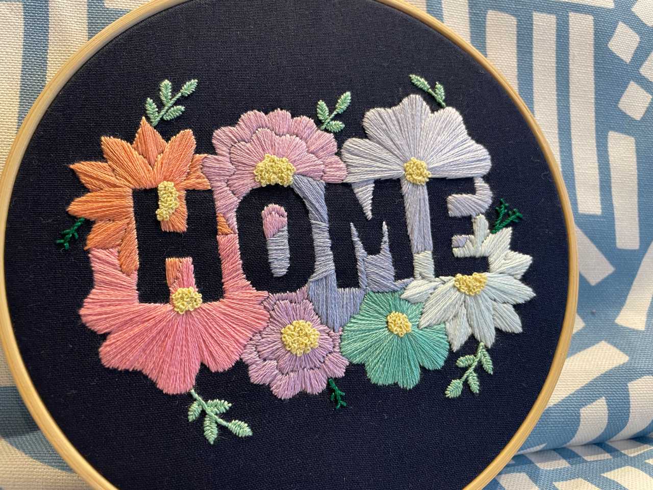 "Home" embroidery hoop utilising a negative space design. Pastel flowers on a dark blue background.