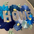 "Home" embroidery hoop utilising a negative space design. Blue flowers on a satin grey background.