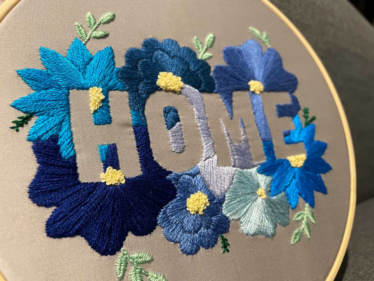 "Home" embroidery hoop utilising a negative space design. Blue flowers on a satin grey background.